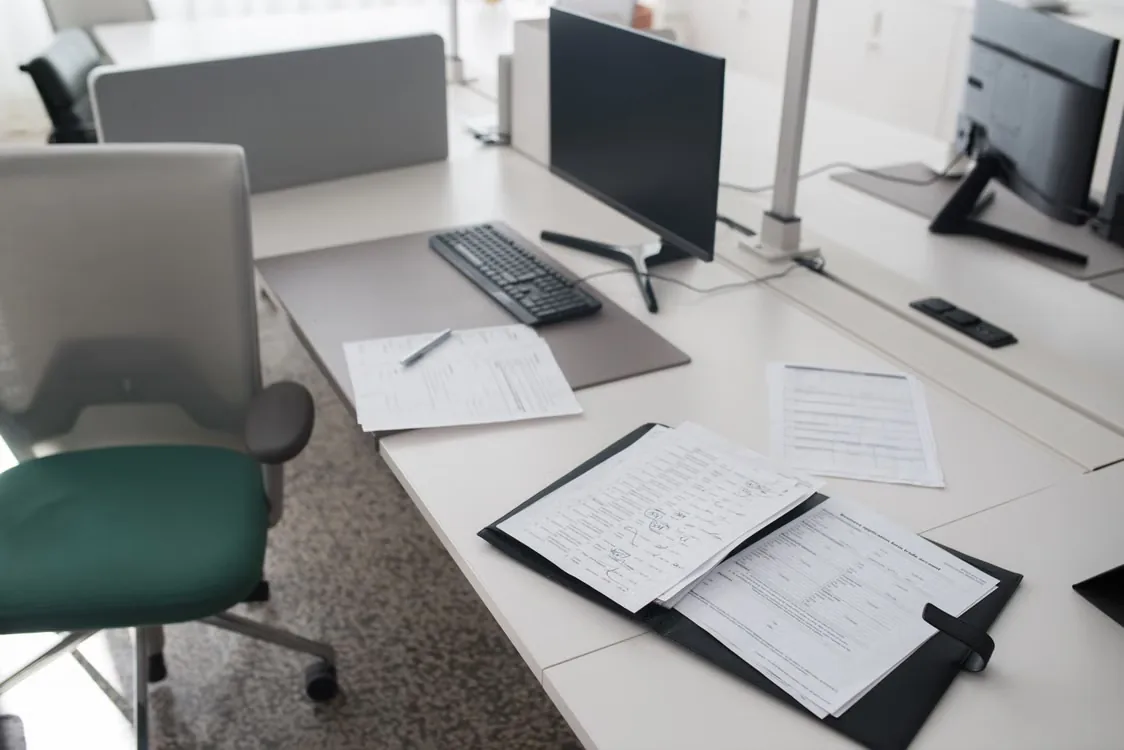 Scrivania ordinata con monitor, tastiera e documenti in un raccoglitore